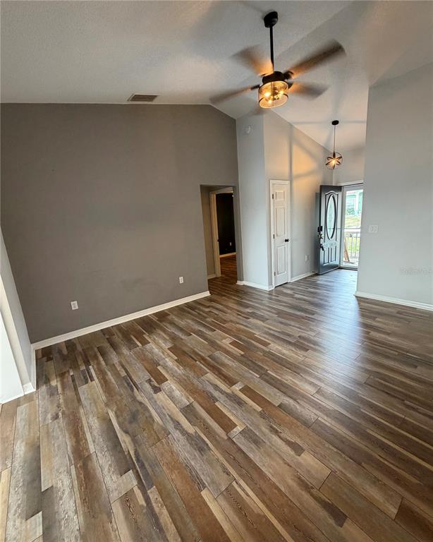A living room with vaulted ceilings, wood-look flooring, a ceiling fan, and an open doorway — 8871 PEBBLEBROOKE DRIVE, LAKELAND, FL