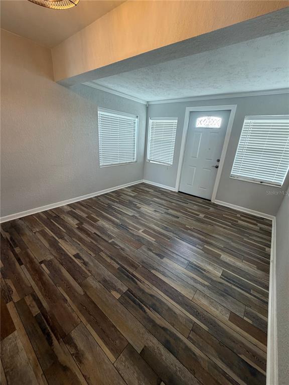 An empty room features wood-look flooring, white walls, three windows with blinds, and a front door — 8871 PEBBLEBROOKE DRIVE, LAKELAND, FL