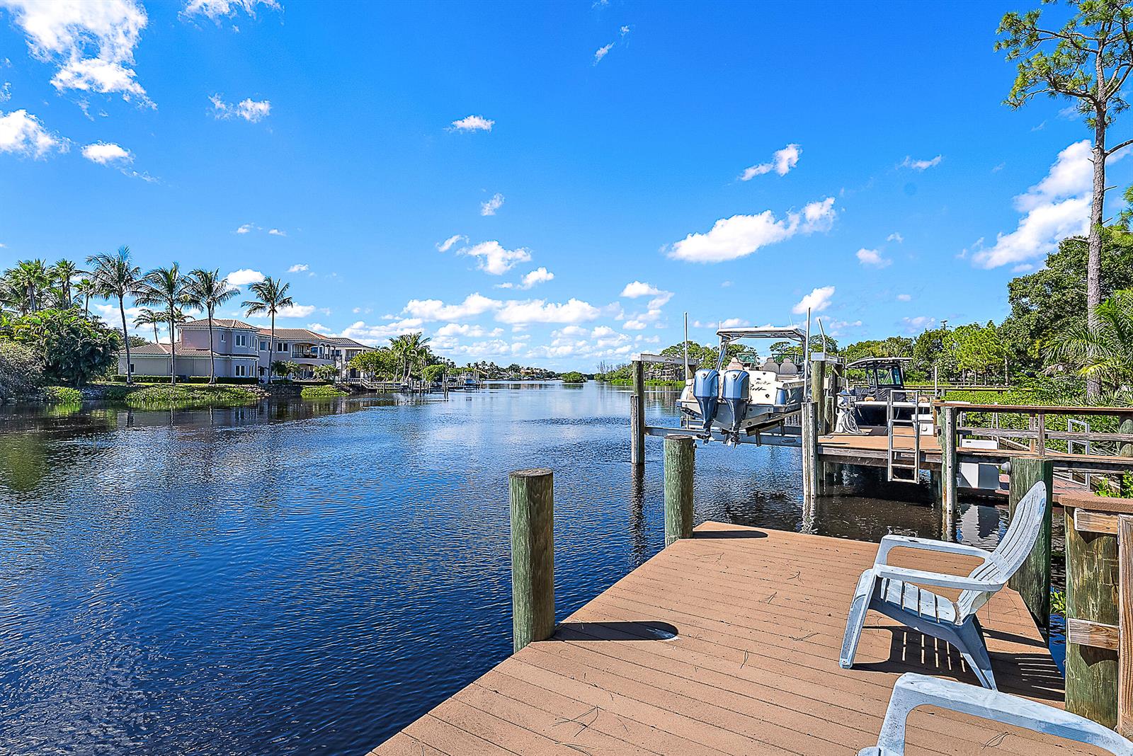 A wooden dock with chairs overlooks a canal with a boat lift and palm trees — 18706 SE St Augustine Way, Jupiter FL 33458, JUPITER, FL