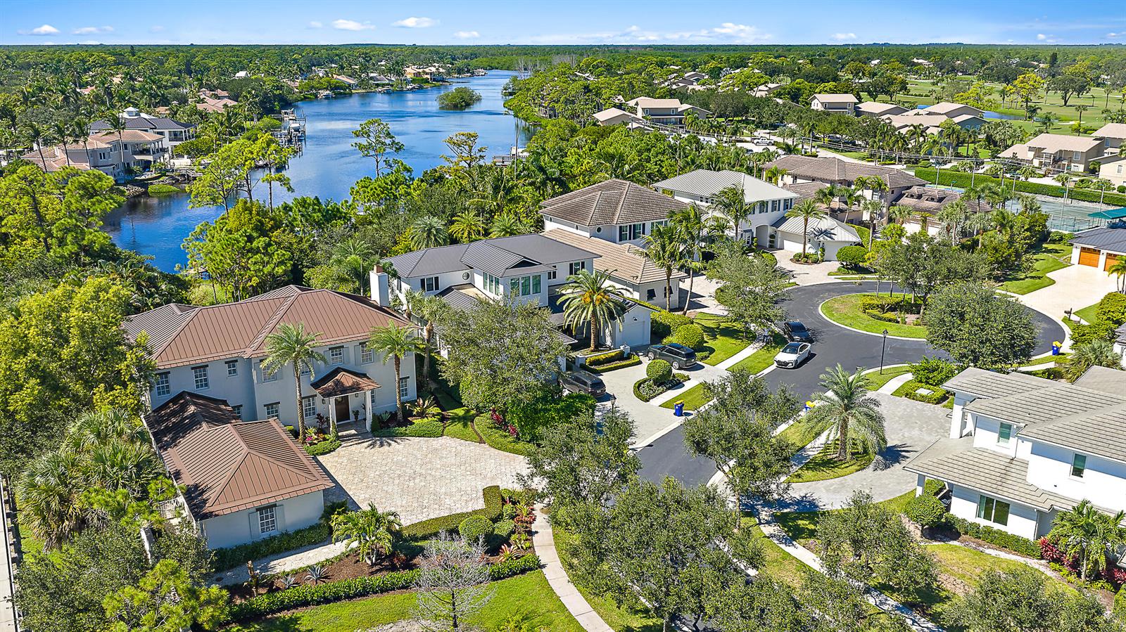 An aerial view shows several large houses with metal roofs situated near a winding canal — 18706 SE St Augustine Way, Jupiter FL 33458, JUPITER, FL
