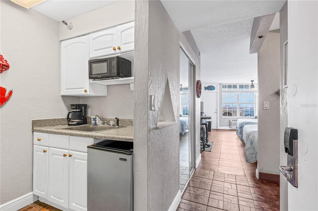 A small kitchenette with white cabinets and a mini-fridge opens into a bedroom area — 313 S ATLANTIC AVENUE UNIT 5310, DAYTONA BEACH, FL