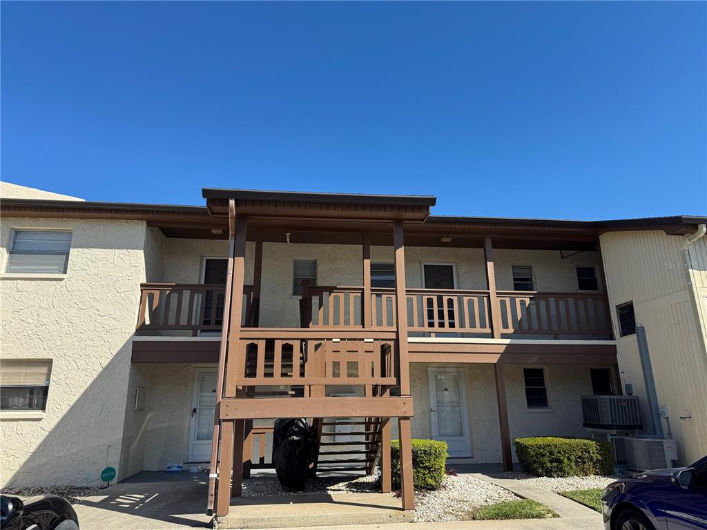A two-story apartment building exterior features a central wooden staircase and balcony — 5154 TURQUOISE LANE UNIT 102, NEW PORT RICHEY, FL