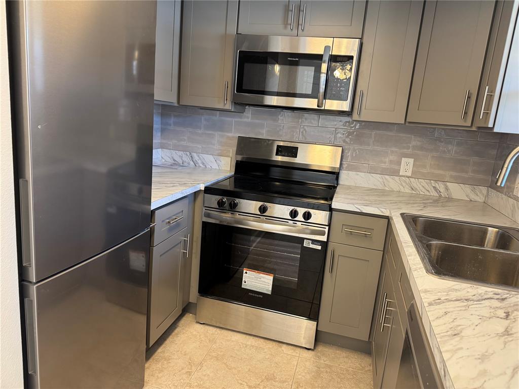 A kitchen featuring stainless steel appliances, gray cabinets, and white marble-patterned countertops — 5154 TURQUOISE LANE UNIT 102, NEW PORT RICHEY, FL