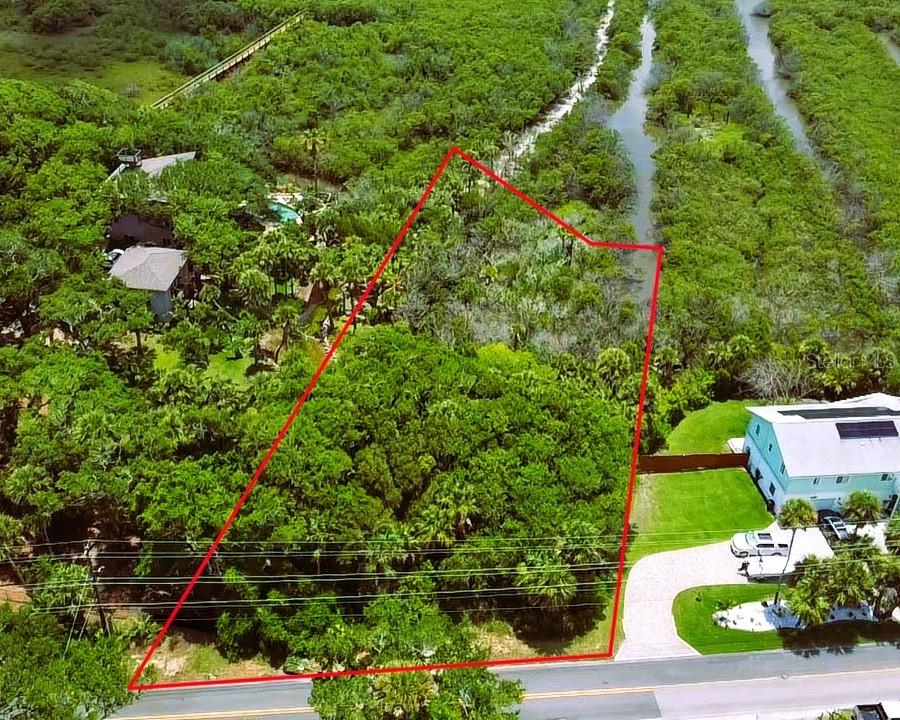 An aerial view shows a vacant, tree-covered lot outlined in red next to two houses — 4168 SAXON DRIVE, NEW SMYRNA BEACH, FL