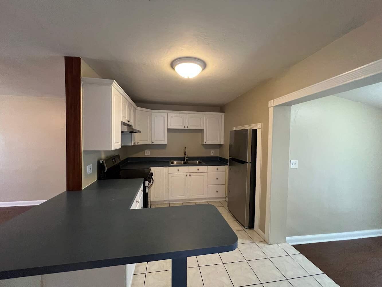 A kitchen features white cabinets, dark countertops, stainless steel appliances, and light-colored floor tiles — DAVIE, FL