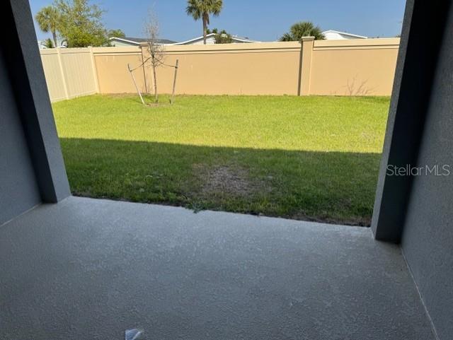 A view from a covered concrete patio looking out onto a grassy backyard with fencing — 3649 YARIAN DRIVE, HAINES CITY, FL