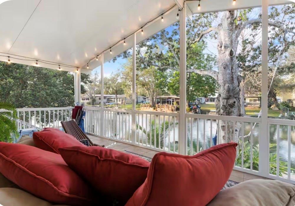 A screened-in porch with red cushions overlooks a canal and large trees — 6331 THEODAN STREET, WEEKI WACHEE, FL