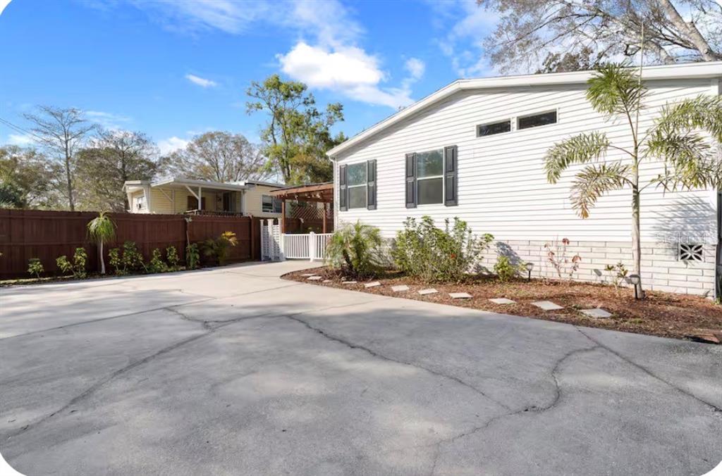 A white mobile home exterior features a concrete driveway, a wooden fence, and landscaping — 6331 THEODAN STREET, WEEKI WACHEE, FL