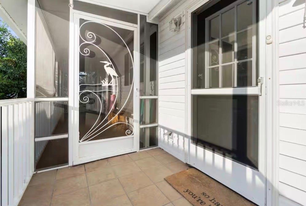 A tiled porch features a white storm door with a decorative heron design and siding — 6331 THEODAN STREET, WEEKI WACHEE, FL