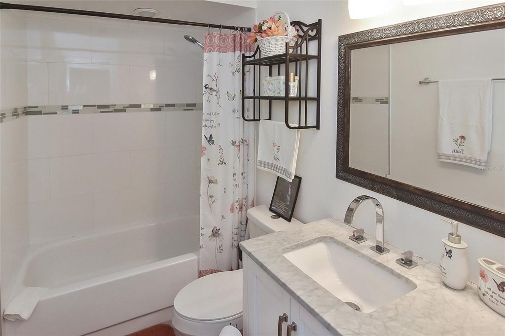 A bathroom features a white vanity with a marble countertop, a shower-tub combo, and a mirror — 1527 STEWART DRIVE UNIT 115, SARASOTA, FL