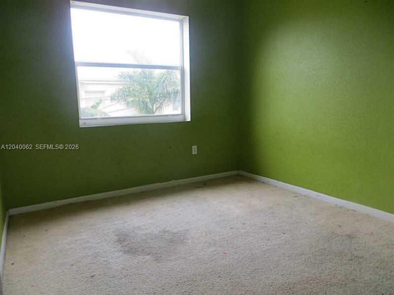 An empty bedroom features green walls, beige carpeting, and a single window — 436 NW 84th Ter # 436, Miami FL 33150, MIAMI, FL