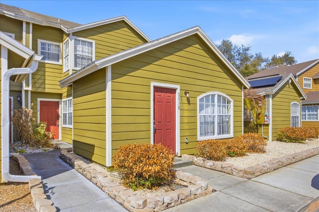 The exterior of two adjacent yellow townhomes with red front doors and stone-bordered landscaping — 2918 FAN PALM DRIVE Front unit, DAVENPORT, FL