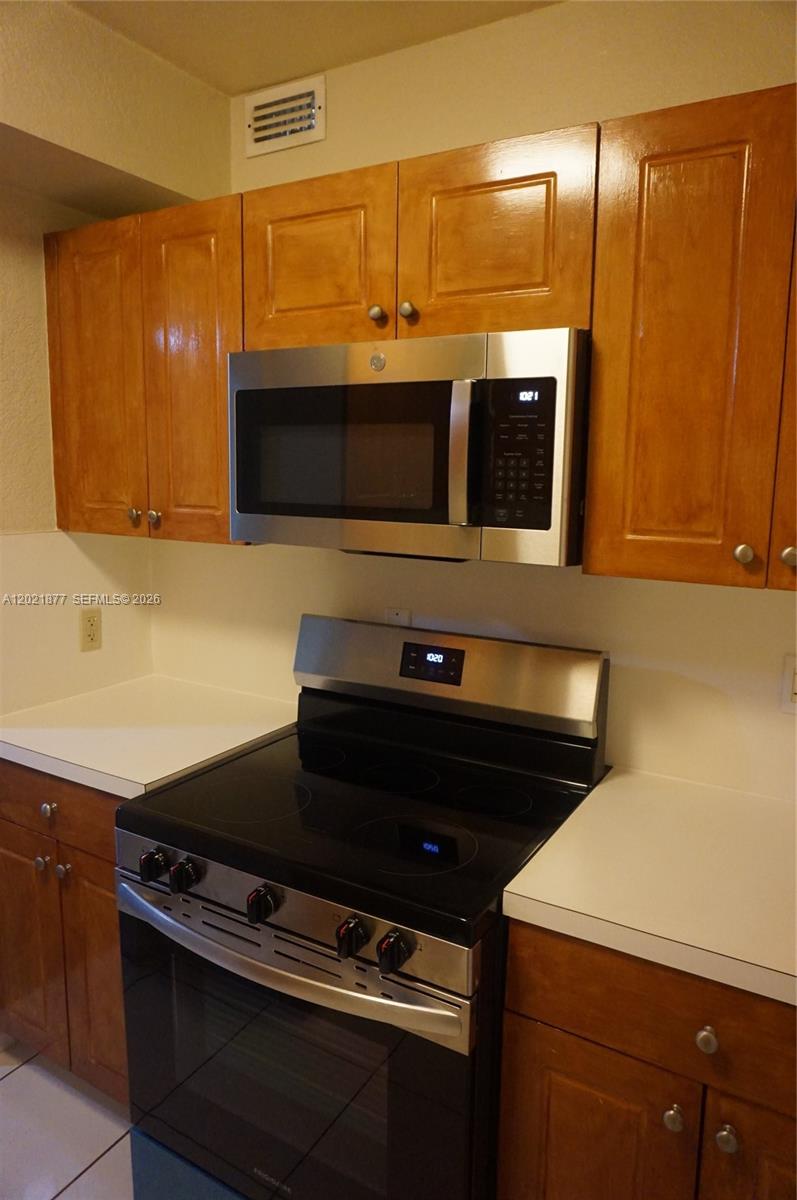 A kitchen features wooden cabinets, a stainless steel microwave, and a black electric range — 770 SE 2nd Ave # A205, Deerfield Beach FL 33441, DEERFIELD BEACH, FL