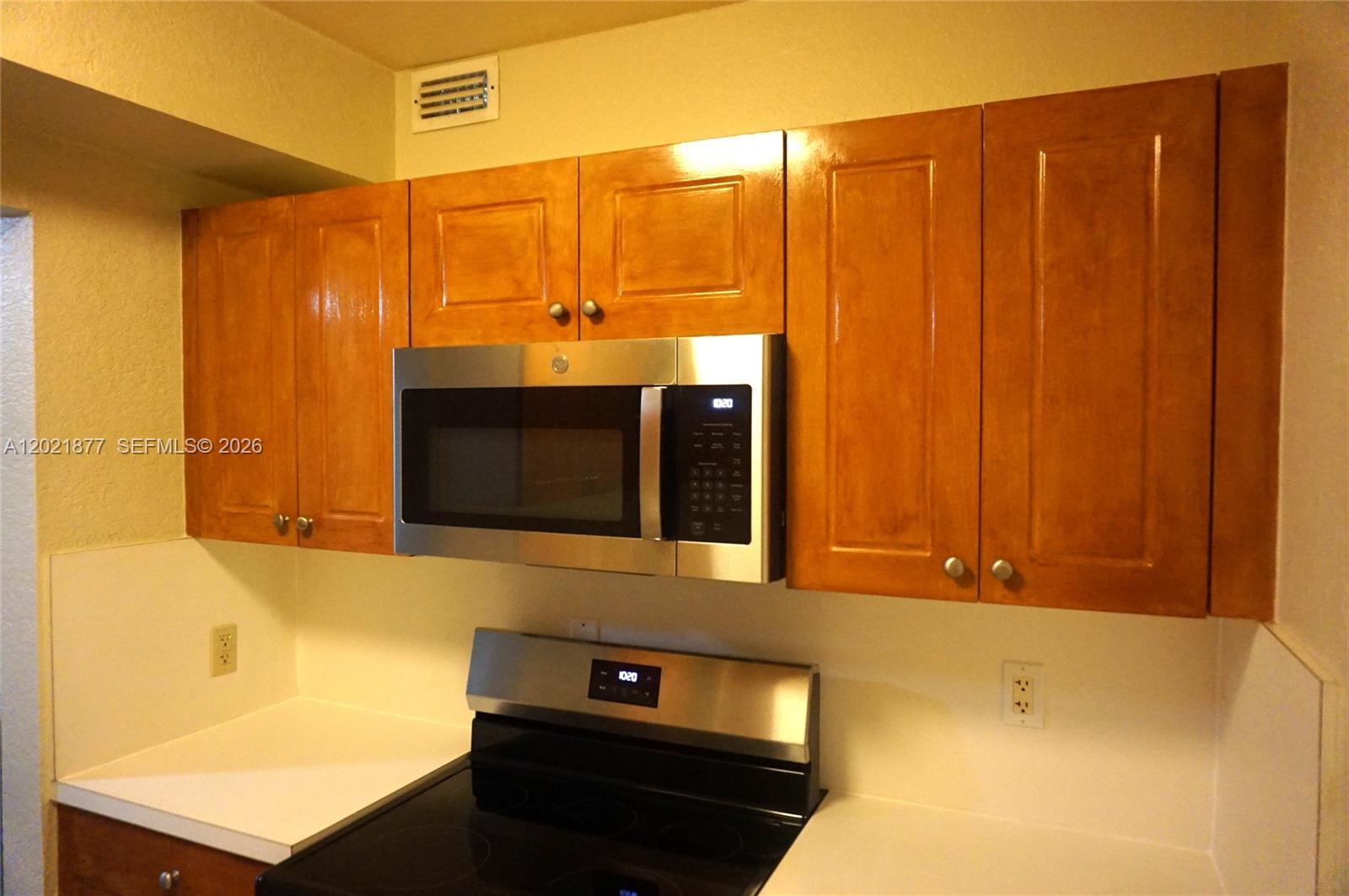 A kitchen features wooden cabinets, a stainless steel microwave, and a black electric stove — 770 SE 2nd Ave # A205, Deerfield Beach FL 33441, DEERFIELD BEACH, FL