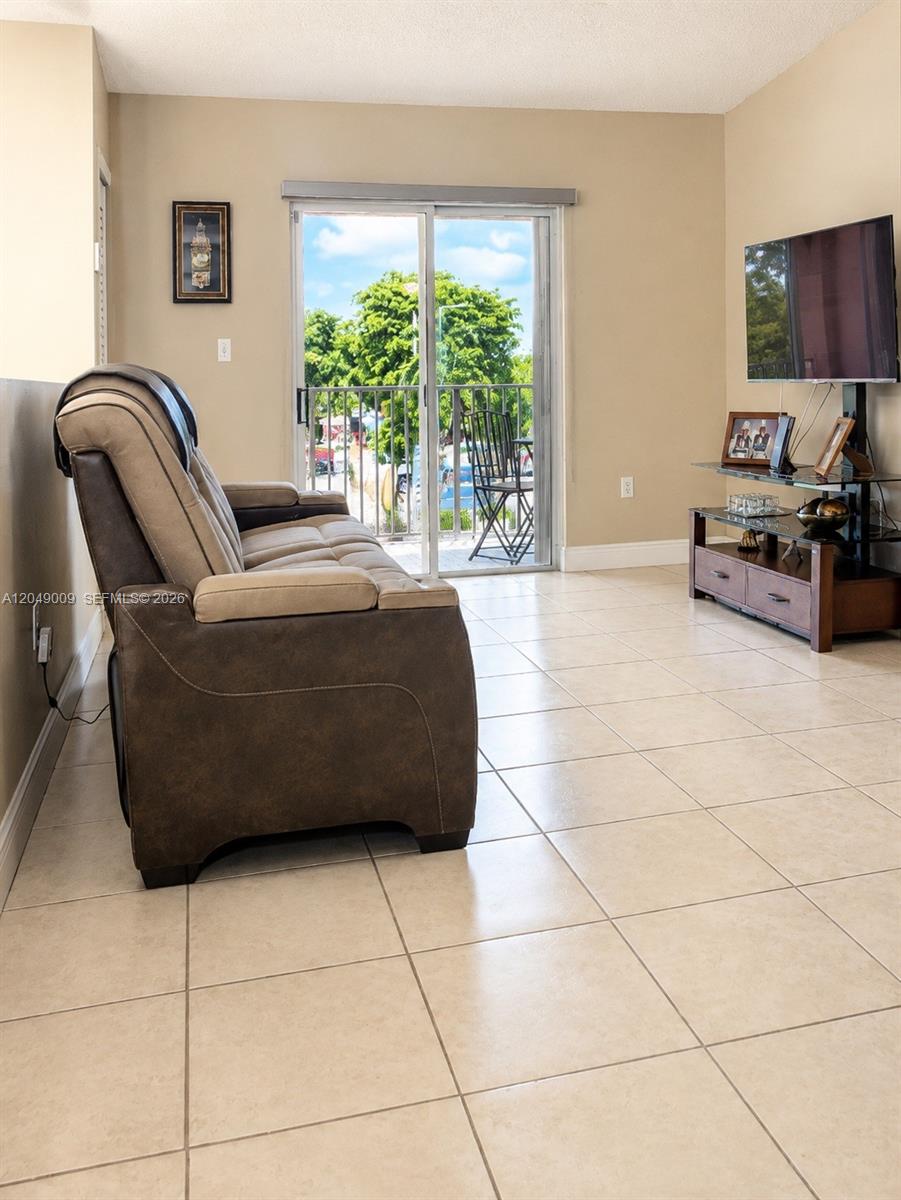 A living room features beige tile floors, a brown recliner, and a sliding glass balcony door — 5800 W 18th Ln, Hialeah FL 33012, HIALEAH, FL