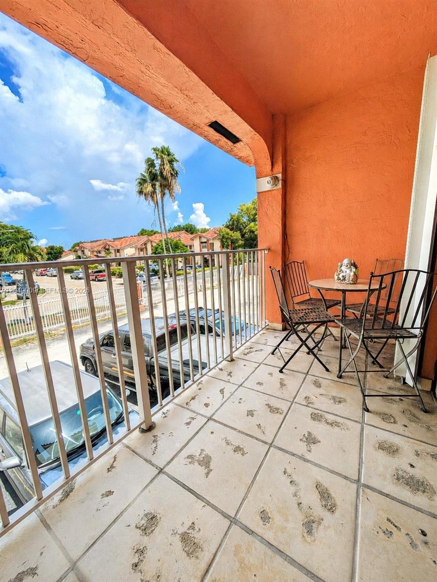 A balcony with a metal table and chairs overlooks a parking lot and palm trees — 5800 W 18th Ln, Hialeah FL 33012, HIALEAH, FL