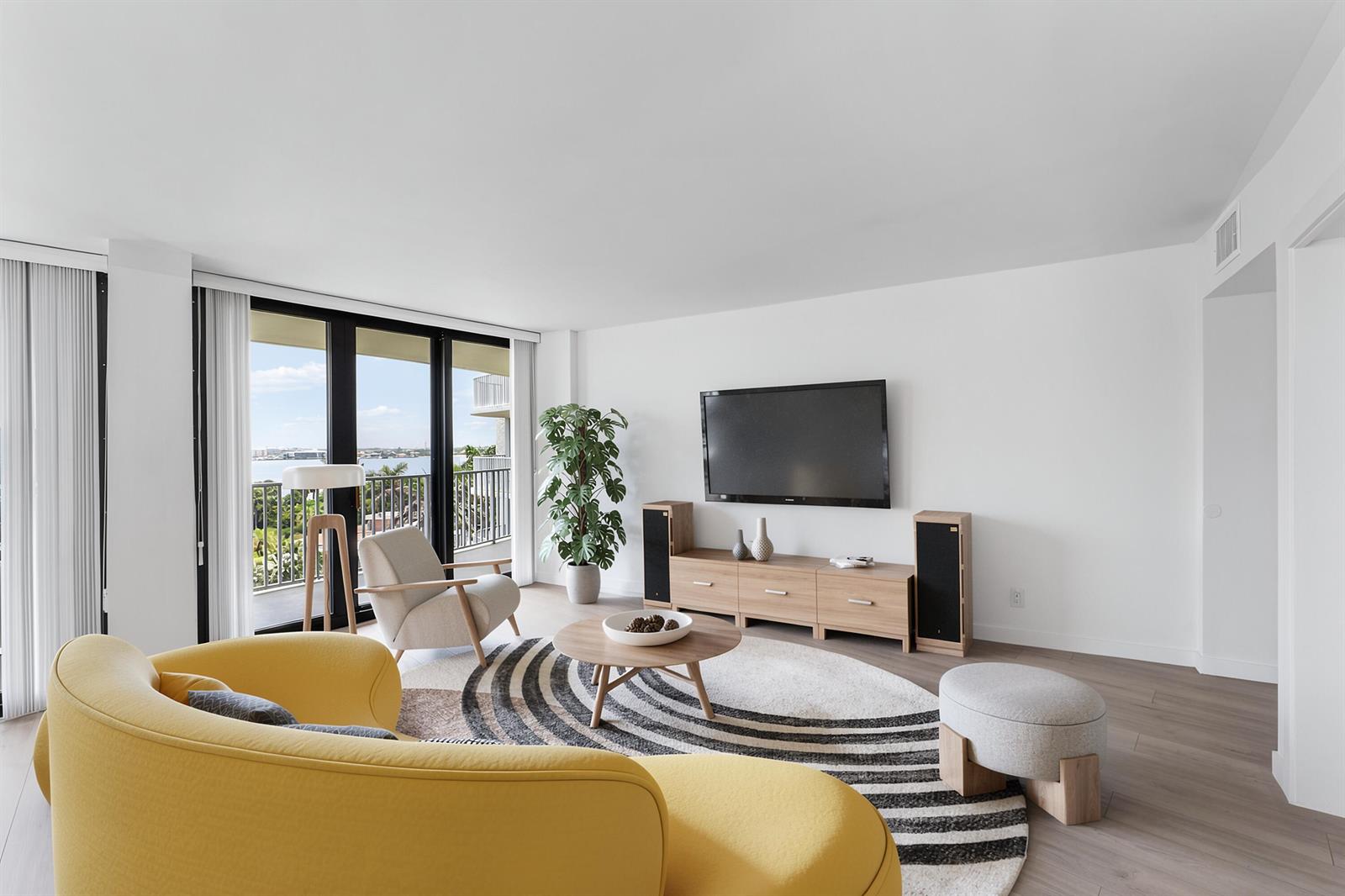 A modern living room features a yellow sofa, circular rug, television, and balcony with water views — 3360 S Ocean Boulevard, Palm Beach FL 33480, PALM BEACH, FL