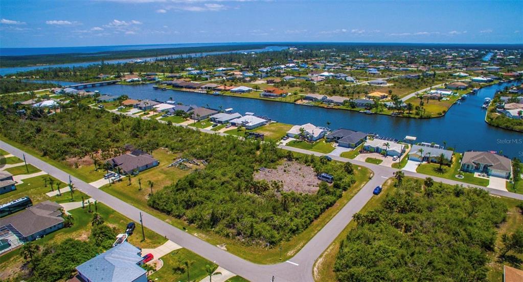 An aerial view shows a vacant, brush-covered residential lot situated near a canal and homes — 15531 AQUA CIRCLE, PORT CHARLOTTE, FL