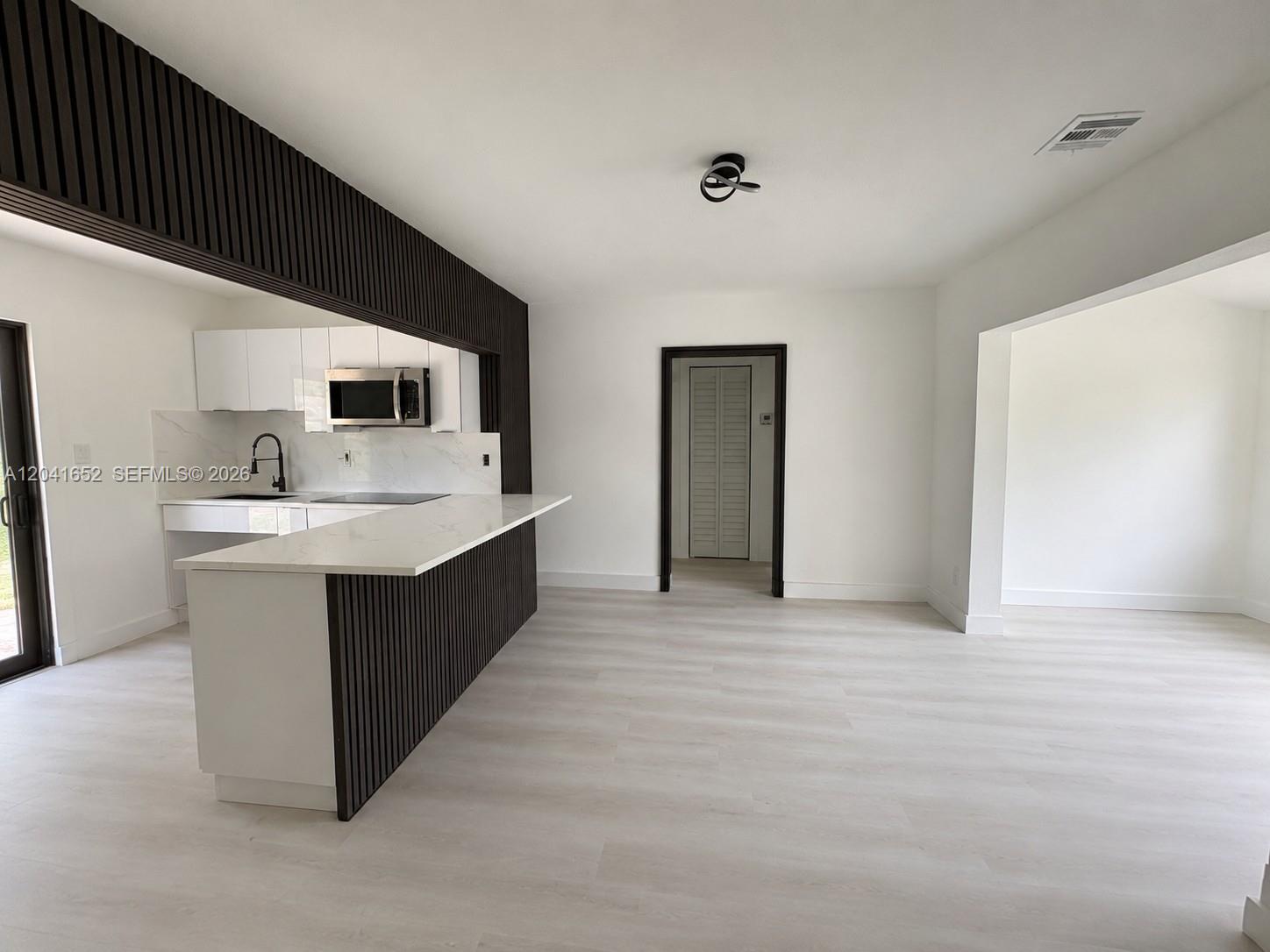 A modern kitchen features white cabinets, a marble-look countertop, and dark wood slat paneling — 811 NW 65th St, Miami FL 33150, MIAMI, FL