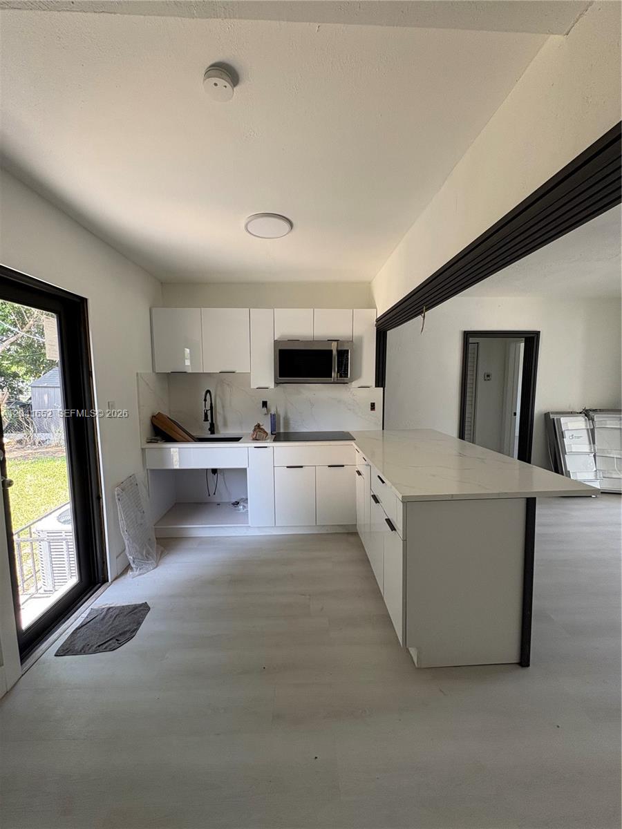 A modern kitchen features white cabinetry, a marble-look countertop, and a peninsula island — 811 NW 65th St, Miami FL 33150, MIAMI, FL