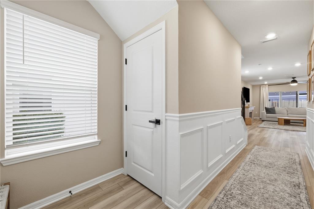 A hallway with white wainscoting, a closed door, and a window leads to a living room — 20958 DRAKE ELM DRIVE, LAND O LAKES, FL