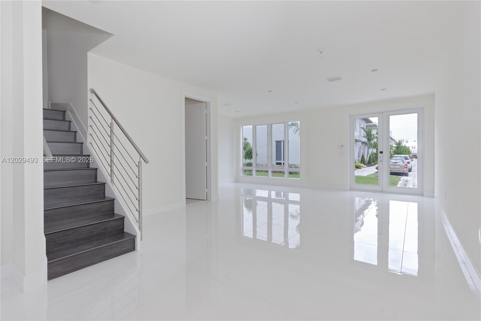 An empty room features white tile floors, a dark wood staircase, and glass doors — DORAL, FL