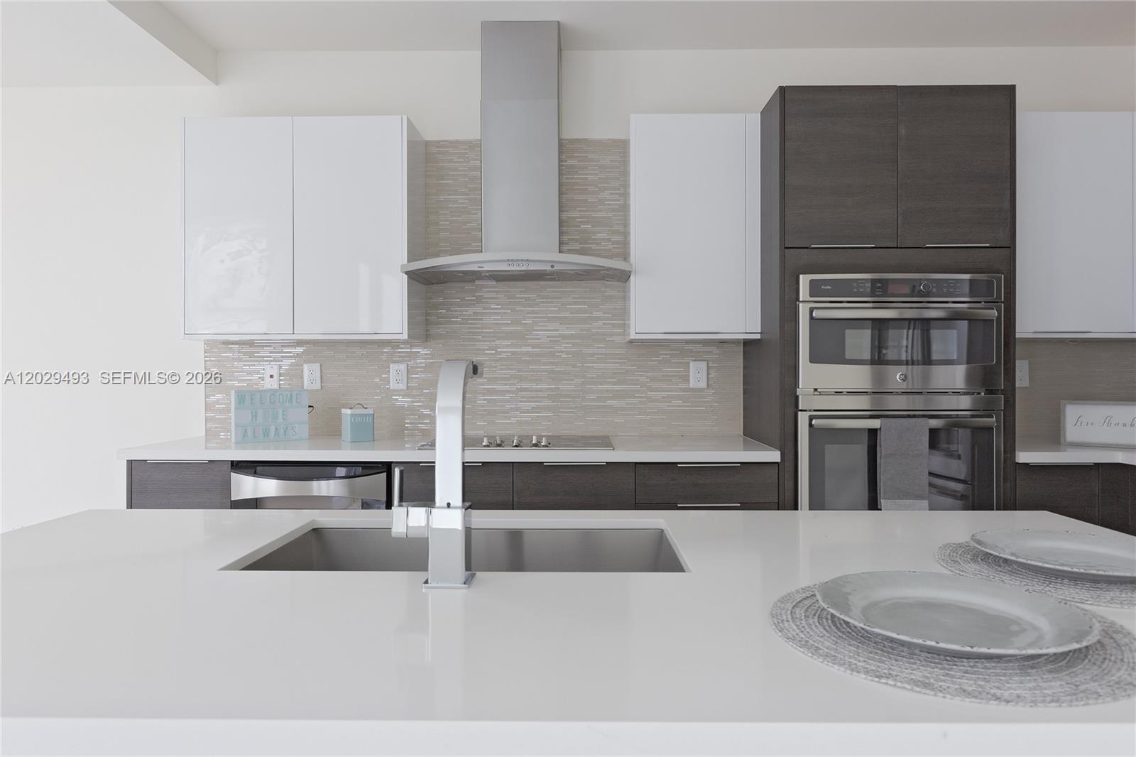 A modern kitchen features white upper cabinets, dark lower cabinets, stainless steel appliances, and a quartz island — DORAL, FL