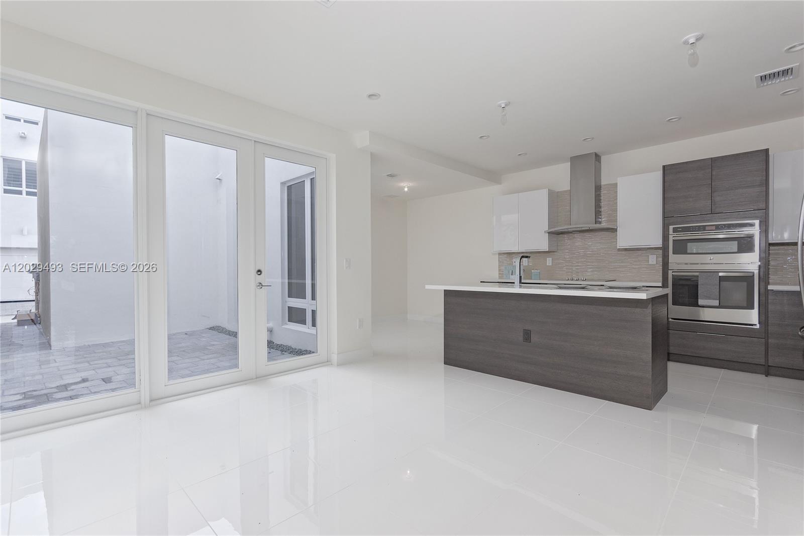 A modern kitchen features a dark wood island, white cabinets, and glass doors to a patio — DORAL, FL