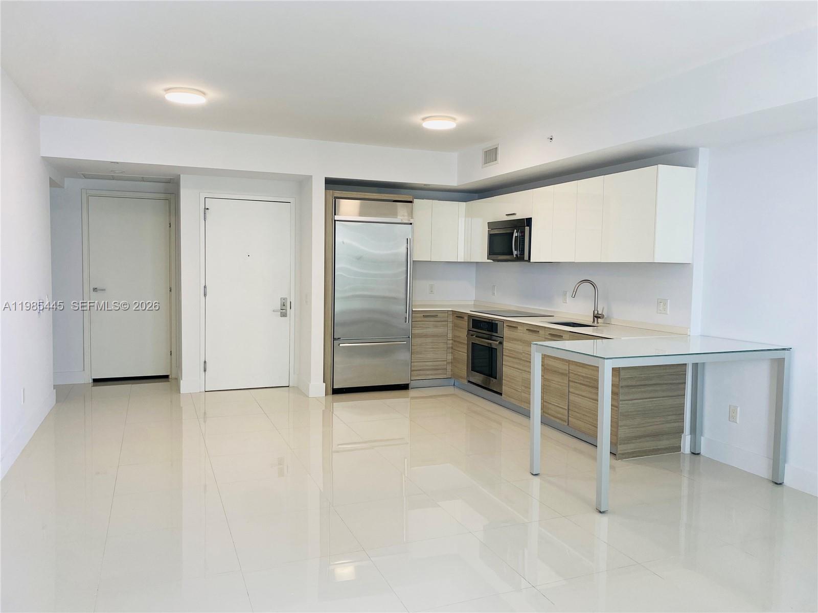 A modern kitchen features stainless steel appliances, wood-grain lower cabinets, white upper cabinets, and tile flooring — 1300 Brickell Bay Dr # 1903, Miami FL 33131, MIAMI, FL