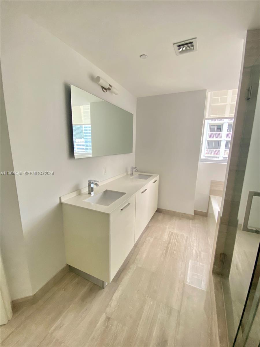 A modern bathroom features a double vanity with white cabinets and a large wall mirror — 1300 Brickell Bay Dr # 1903, Miami FL 33131, MIAMI, FL
