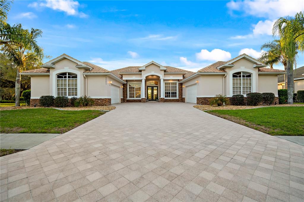 A single-story house with a paved driveway, tan stucco exterior, and two attached garages — 5021 CHAMPIONSHIP CUP LANE, SPRING HILL, FL