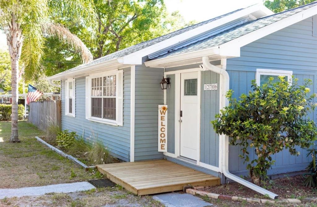 A blue house with white trim features a wooden front deck and a welcome sign — 12706 FOREST STREET, TAMPA, FL