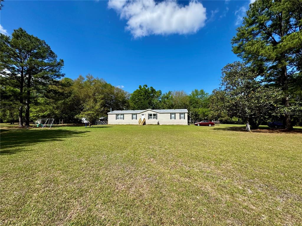 A single-story manufactured home sits in the center of a large, grassy, tree-lined lot — 7222 NW 205TH TERRACE, ALACHUA, FL