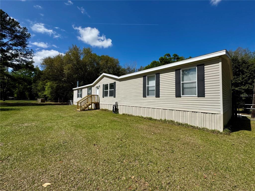 A single-story manufactured home with beige siding and a wooden entrance staircase — 7222 NW 205TH TERRACE, ALACHUA, FL