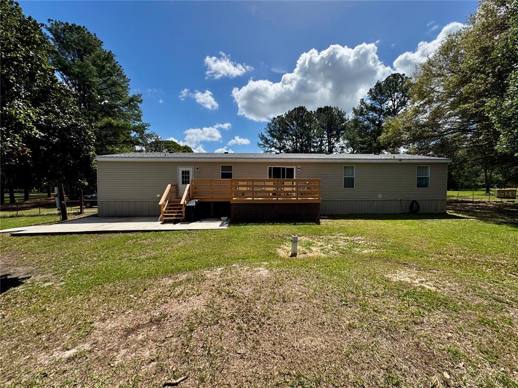The rear exterior of a single-story manufactured home features a wooden deck and concrete patio — 7222 NW 205TH TERRACE, ALACHUA, FL
