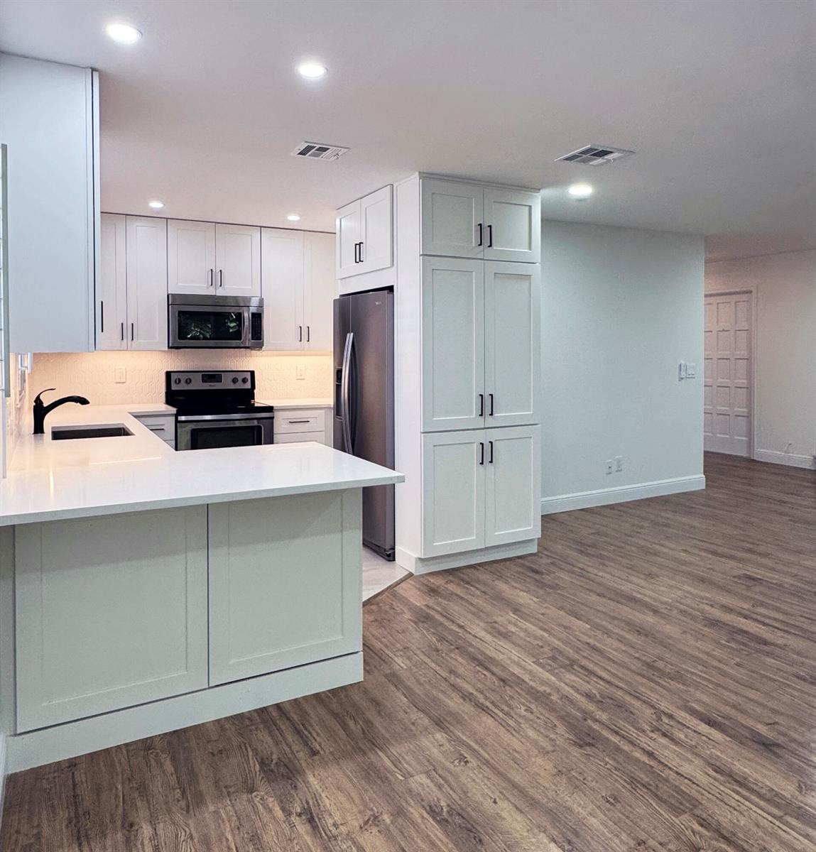 A modern kitchen features white cabinetry, stainless steel appliances, and a peninsula with quartz countertops — 419 Pine Tree Court # 19, Atlantis FL 33462, ATLANTIS, FL