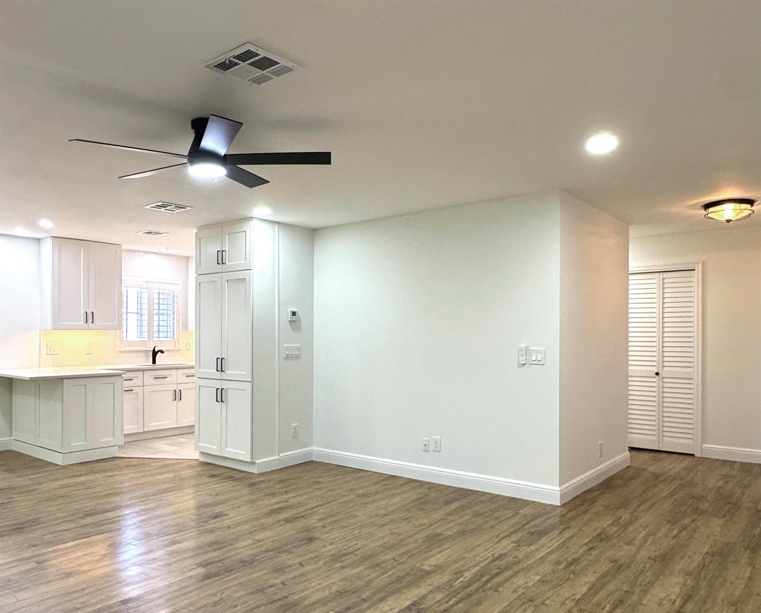 A bright, open-concept room features white kitchen cabinetry, a ceiling fan, and wood-look flooring — 419 Pine Tree Court # 19, Atlantis FL 33462, ATLANTIS, FL