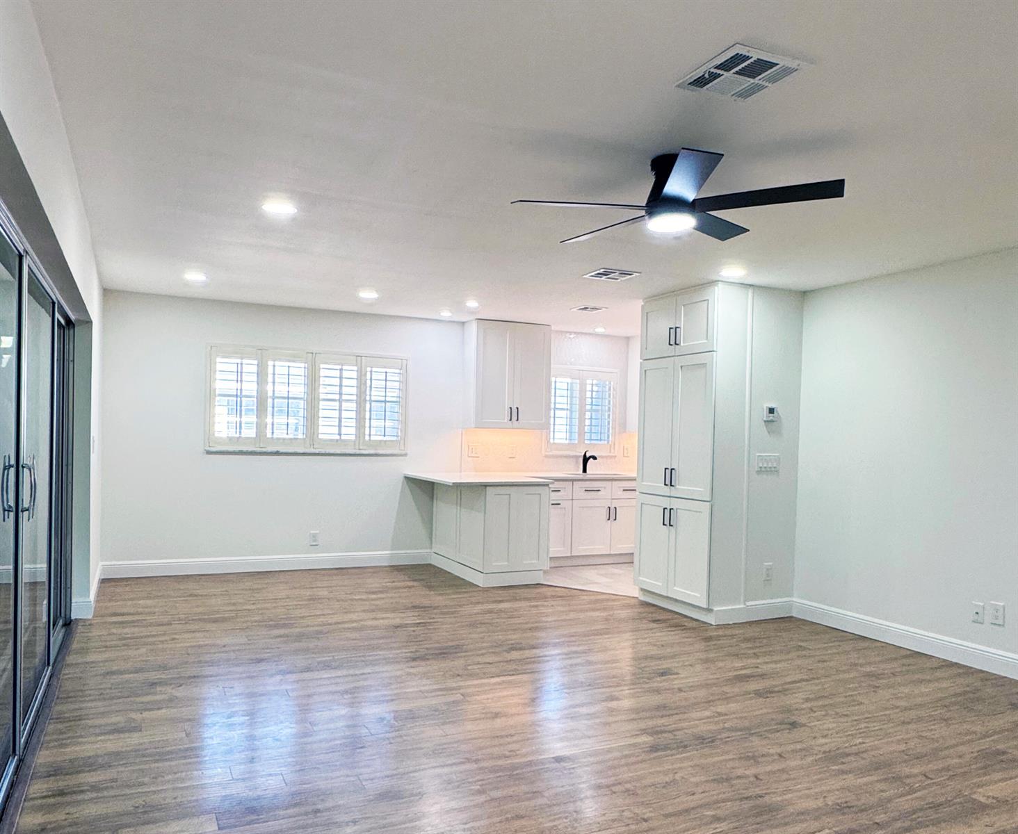 A bright, open-concept kitchen and living area features white cabinetry, wood-look flooring, and a ceiling fan — 419 Pine Tree Court # 19, Atlantis FL 33462, ATLANTIS, FL