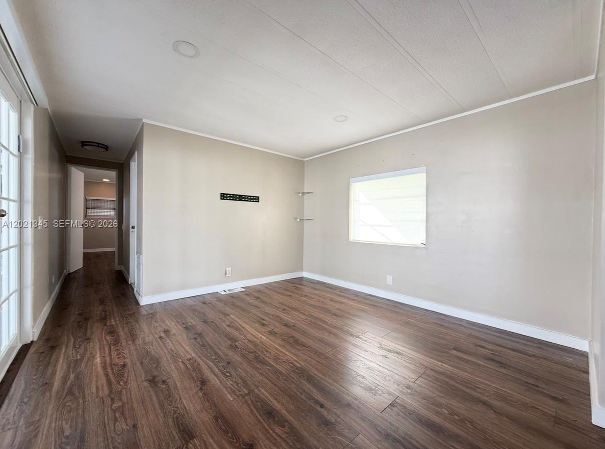 An empty room features wood-look laminate flooring, beige walls, a window, and a hallway entrance — 1332 S 33 AVE, Hollywood FL 33021, HOLLYWOOD, FL