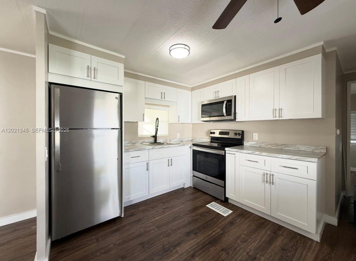 A kitchen features white cabinets, stainless steel appliances, marble-look countertops, and dark wood flooring — 1332 S 33 AVE, Hollywood FL 33021, HOLLYWOOD, FL
