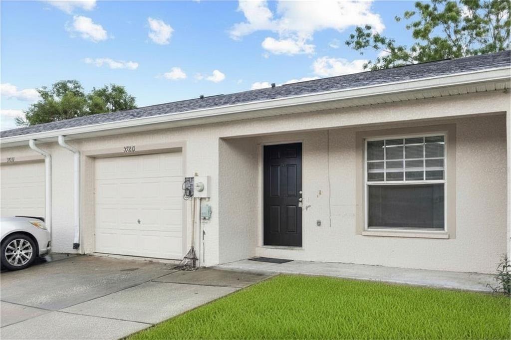 A single-story residential unit features a white stucco exterior, a black front door, and a garage — 37210 GRASSY HILL LANE, DADE CITY, FL