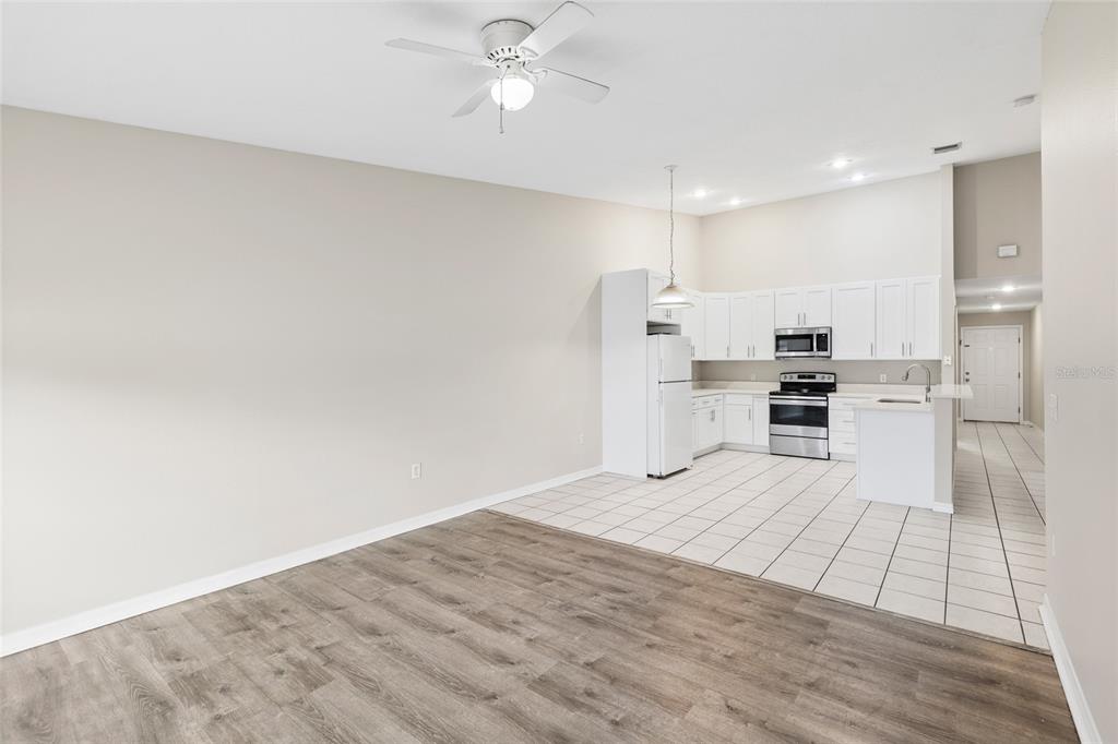 A kitchen with white cabinets and stainless steel appliances opens to a wood-floored living area — 37210 GRASSY HILL LANE, DADE CITY, FL