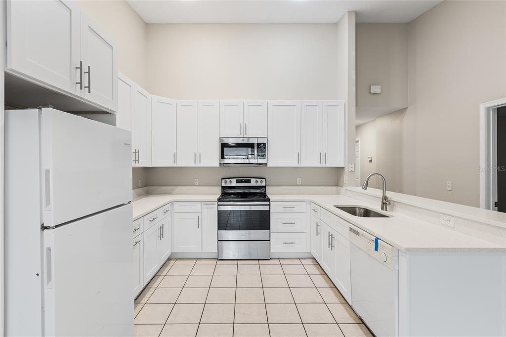 A kitchen features white cabinetry, stainless steel appliances, light countertops, and beige tile flooring — 37210 GRASSY HILL LANE, DADE CITY, FL