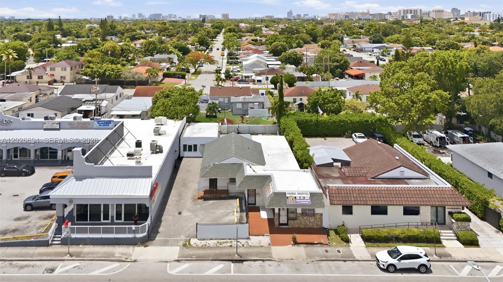 An aerial view shows three commercial buildings along a street with parking and surrounding trees — 3240 NW 7th St, Miami FL 33125, MIAMI, FL