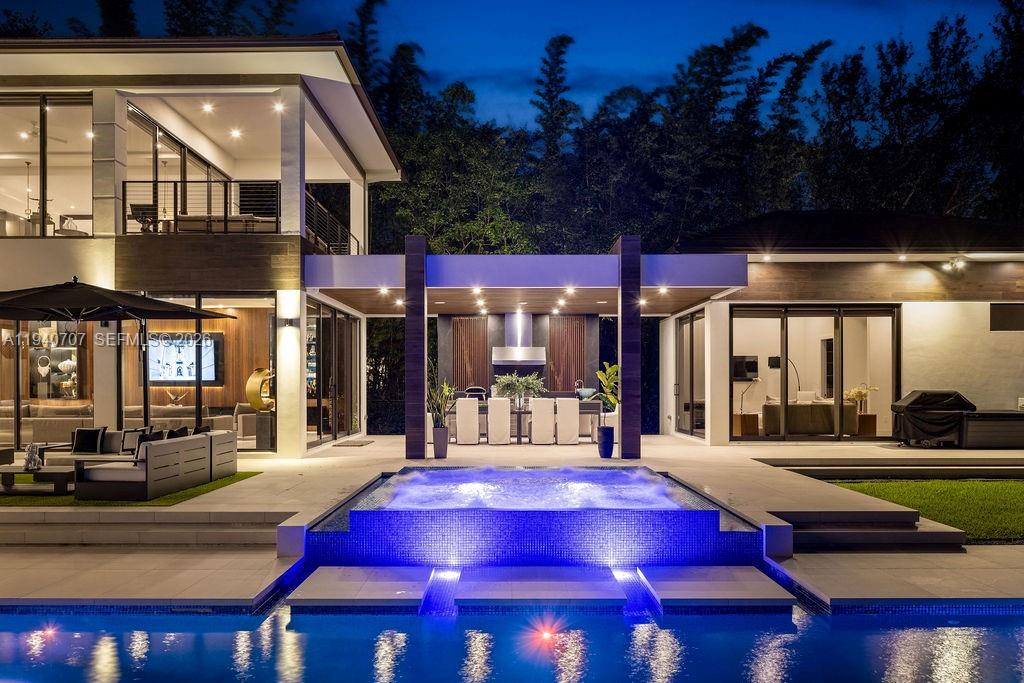 A modern house exterior at night featuring a swimming pool, hot tub, and covered patio — 6850 SW 73rd Ct, Miami FL 33143, MIAMI, FL