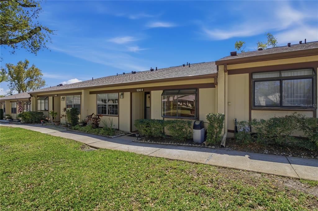 A single-story residential building with tan siding, brown trim, and a concrete walkway — 11241 DOLLAR LAKE DRIVE UNIT 4, PORT RICHEY, FL