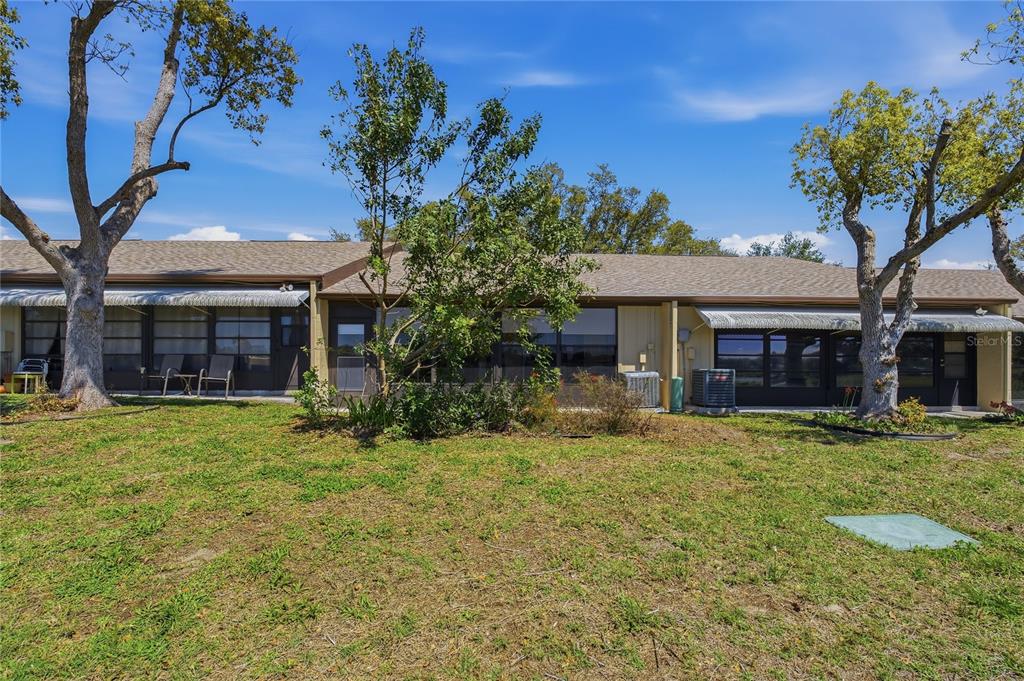 The exterior rear view of a single-story residential building with a grassy lawn and trees — 11241 DOLLAR LAKE DRIVE UNIT 4, PORT RICHEY, FL