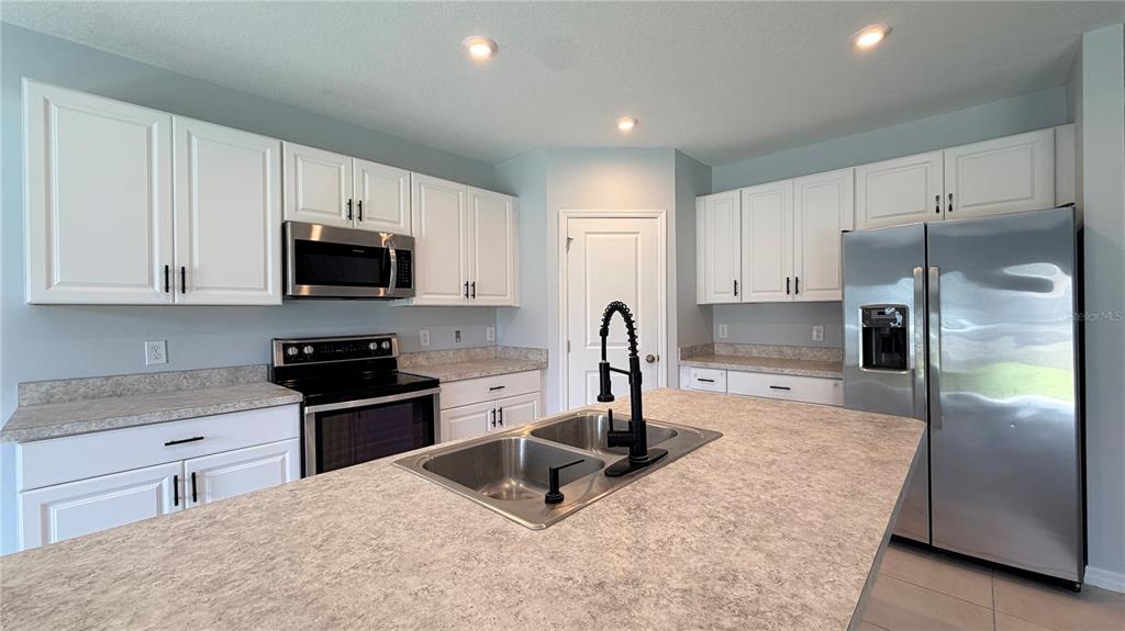 A kitchen features white cabinets, stainless steel appliances, a center island, and laminate countertops — 2811 PARKFIELD ROAD, ST CLOUD, FL