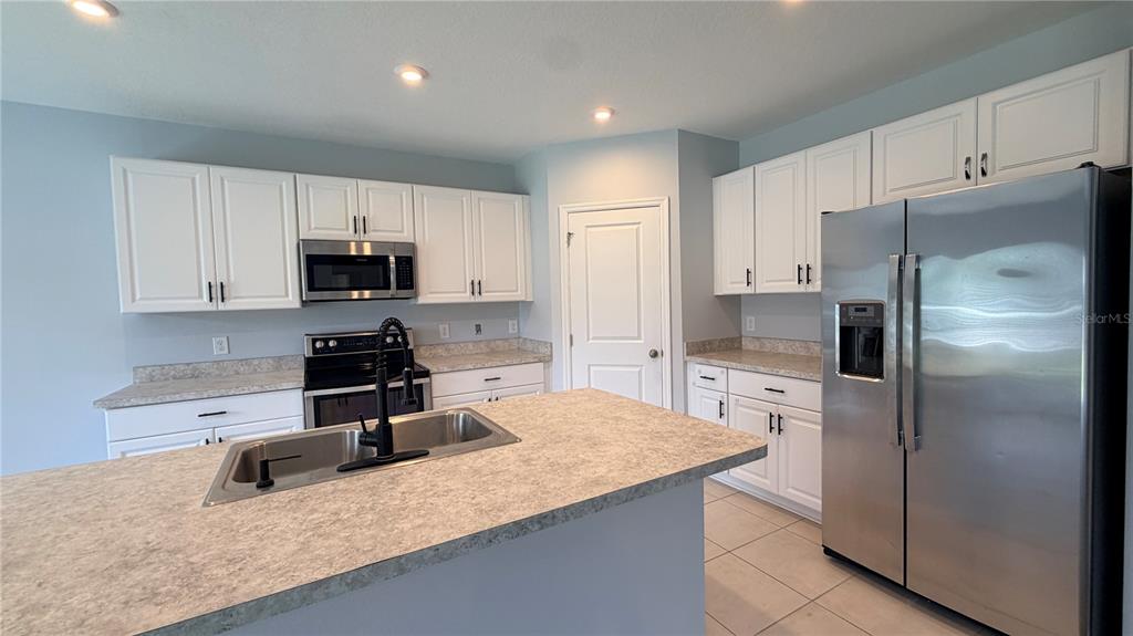 A kitchen features white cabinets, stainless steel appliances, a center island, and light countertops — 2811 PARKFIELD ROAD, ST CLOUD, FL