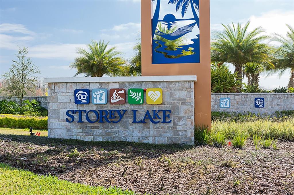 The entrance sign for Storey Lake features a stone wall with colorful icons and landscaping — 2790 OXYMORON WAY, KISSIMMEE, FL